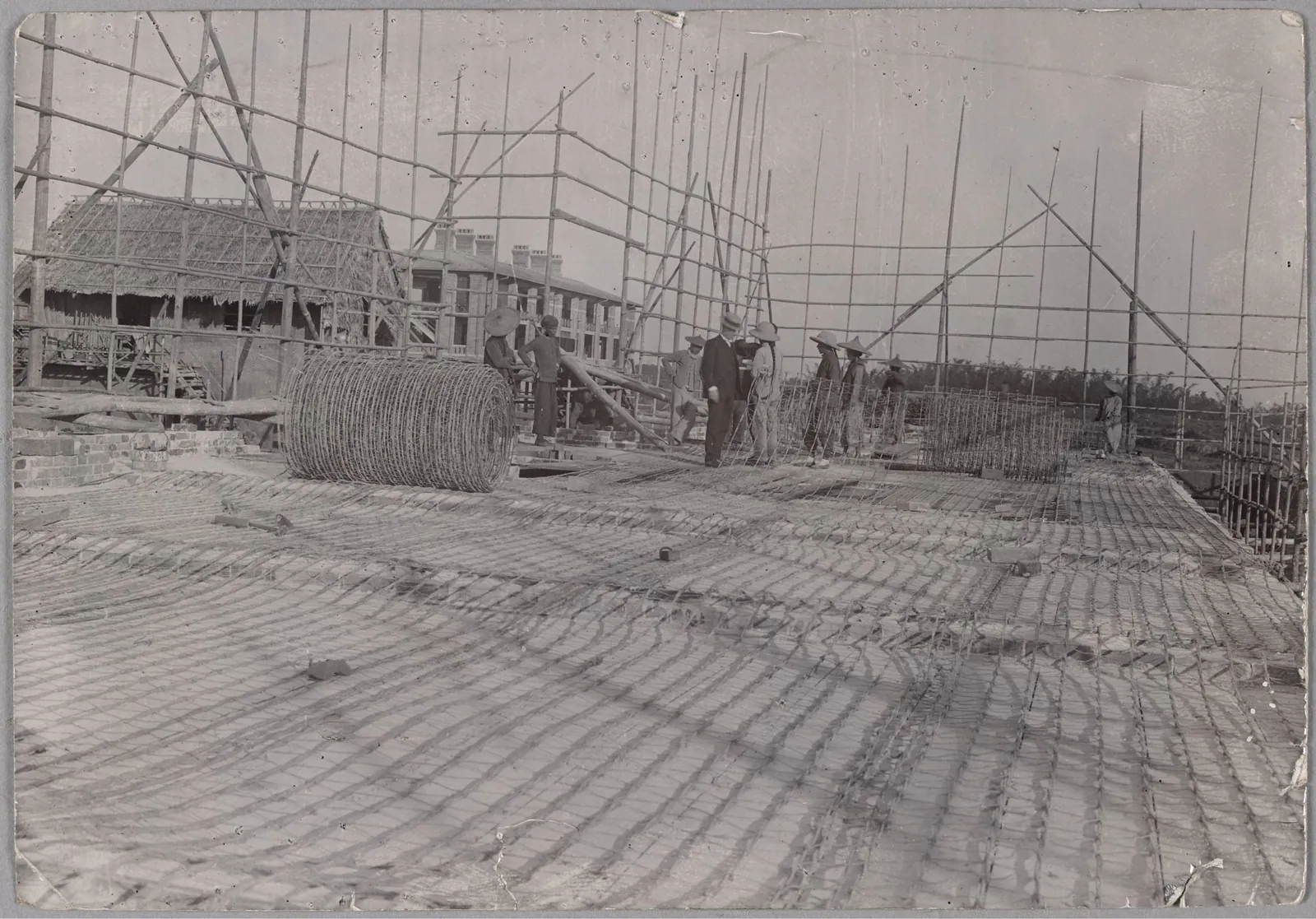 A wide floor of steel mesh laid out under bamboo scaffolding, with workmen standing on it.