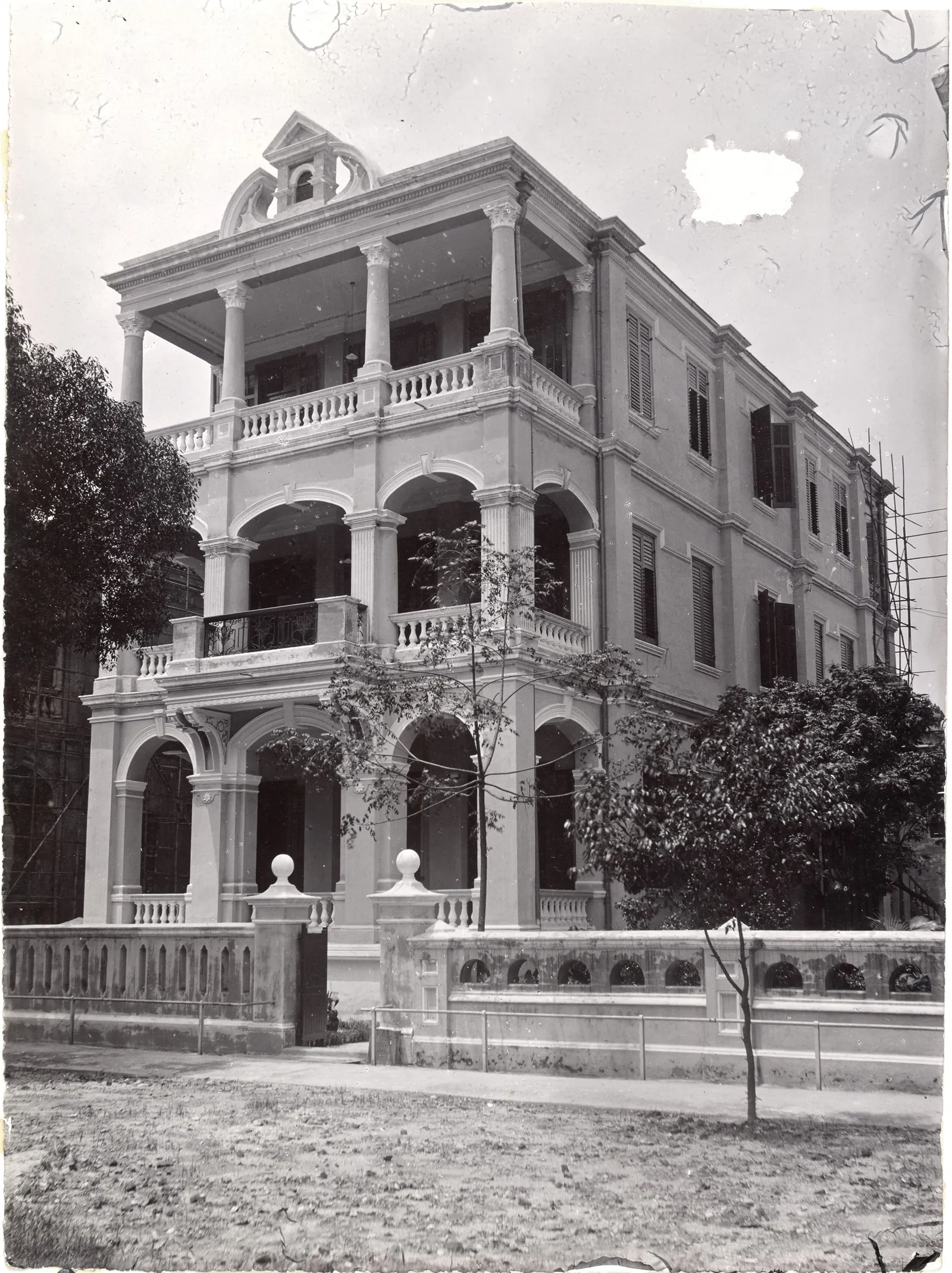 A three-storey house with an arcaded verandah on each floor and an open colonnaded top floor, behind a wall pierced with oval holes.